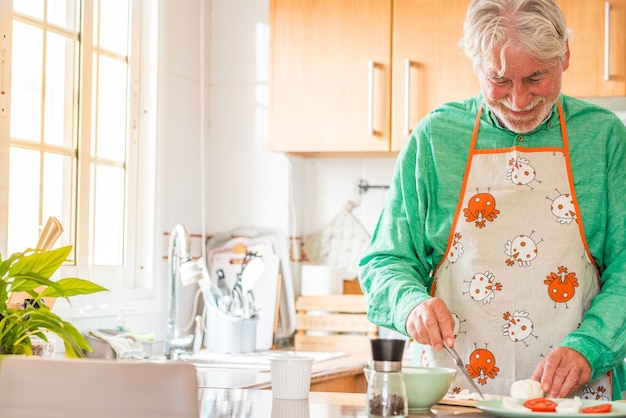 Retrato de um homem maduro e velho cozinhando em casa na cozinha sorrindo. sênior preparando comida para almoçar sozinho dentro de casa. cozinheiro aposentado aprendendo