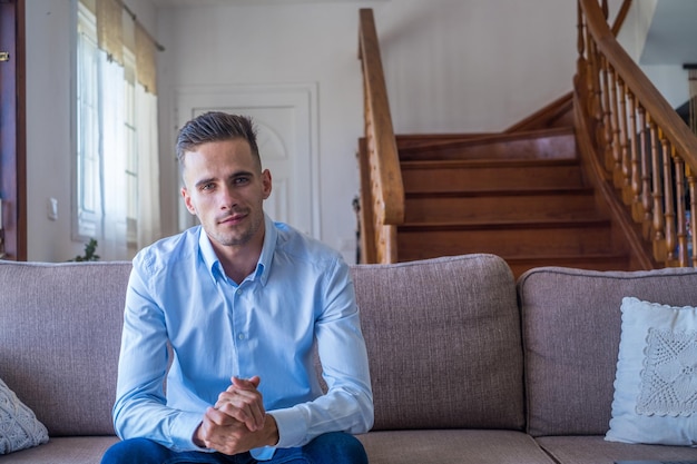 Foto retrato de um homem millennial feliz olhando para a câmera relaxando em casa espaço de cópia homem confiante fazendo foto sentado no sofá no apartamento close upxa