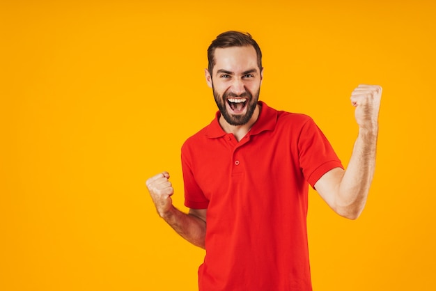 Retrato de um homem moreno em uma camiseta vermelha regozijando-se e gesticulando com triunfo isolado sobre o amarelo