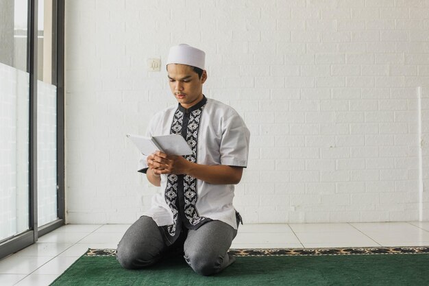 Retrato de um homem muçulmano religioso vestindo uma camisa koko lendo o Alcorão seriamente na mesquita