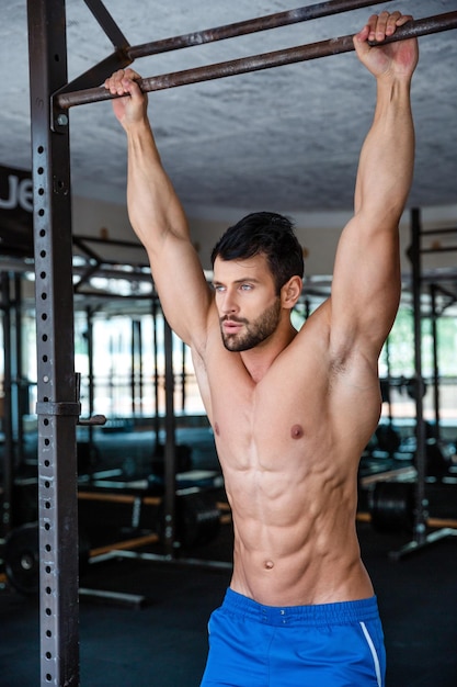 Retrato de um homem musculoso apertando a barra horizontal na academia