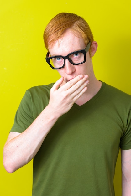 Retrato de um homem nerd com cabelo vermelho, usando óculos e cobrindo a boca