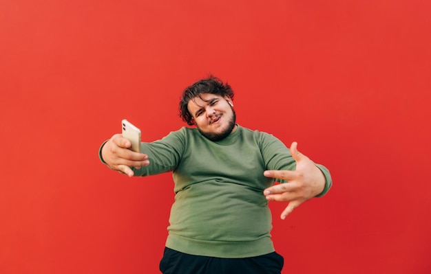 Foto retrato de um homem obeso encaracolado positivo em um fundo vermelho dançando com um sorriso no rosto