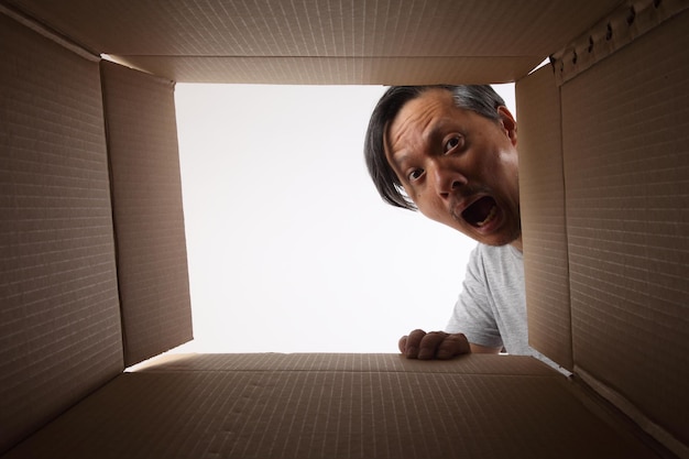 Foto retrato de um homem olhando através de uma caixa de papelão contra um céu claro