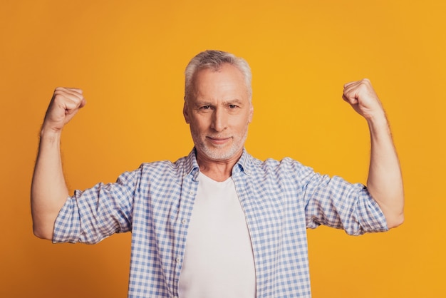 Retrato de um homem orgulhoso de cabelos grisalhos mostrando bíceps isolados sobre o fundo