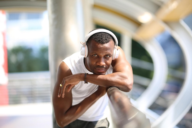 Foto retrato de um homem ouvindo música através de fones de ouvido enquanto está de pé em uma ponte pedonal