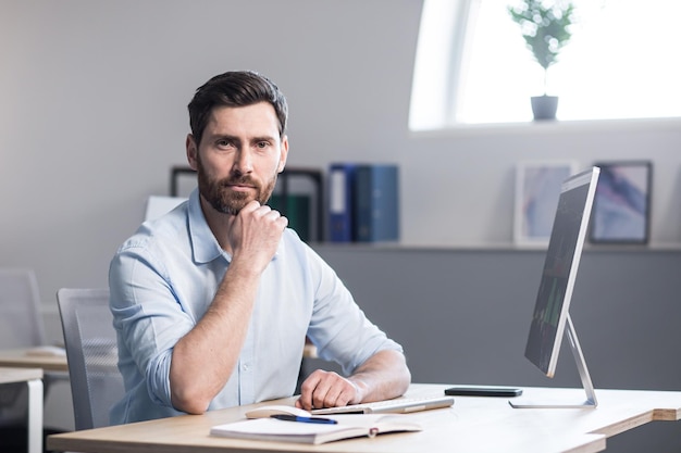 Retrato de um homem pensativo de empresário bem sucedido e sério olhando para a câmera trabalhando no escritório no computador