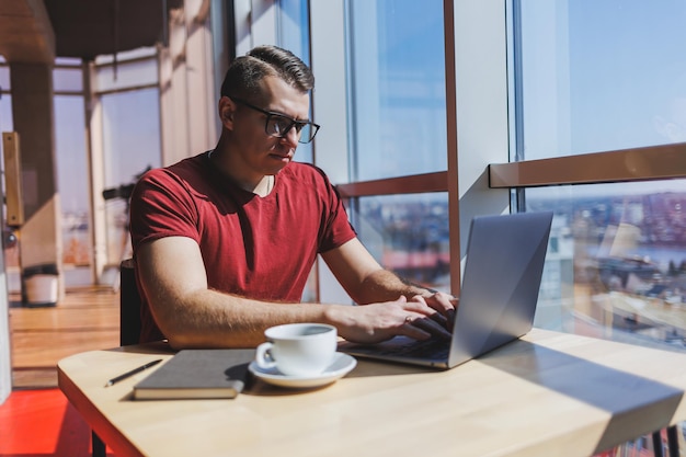 Retrato de um homem profissional de TI trabalhando remotamente com um laptop moderno sentado em uma mesa e sorrindo para a câmera durante um intervalo um programador humano feliz em óculos de correção de visão