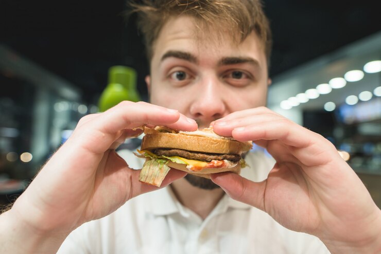 Foto retrato de um homem que morde um hambúrguer e olhando para a câmera. comer fast food. hambúrguer na boca