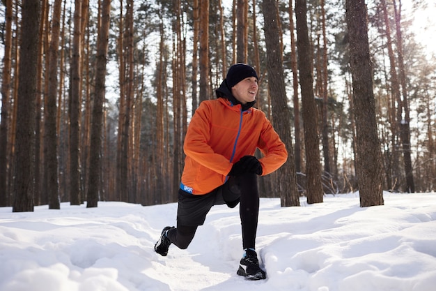 Retrato de um homem se alongando no parque em um lindo dia de neve de inverno, preparando-se para correr