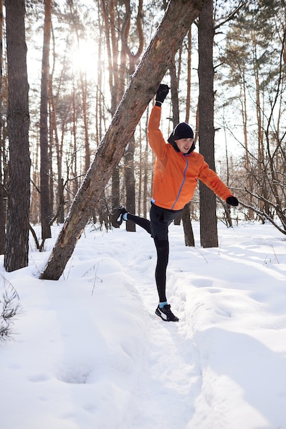 Retrato de um homem se alongando no parque em um lindo dia de neve de inverno, preparando-se para correr