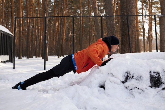 Retrato de um homem se alongando no parque em um lindo dia de neve de inverno, preparando-se para correr