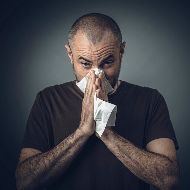 Retrato de um homem segurando papel de tecido sobre o nariz contra um fundo cinzento