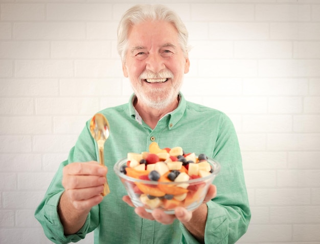 Foto retrato de um homem sênior alegre pronto para comer uma salada de frutas frescas de verão avô idoso segurando uma tigela de vidro com comida saudável