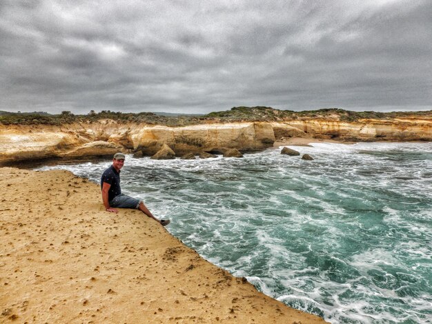 Foto retrato de um homem sentado na praia contra um céu nublado