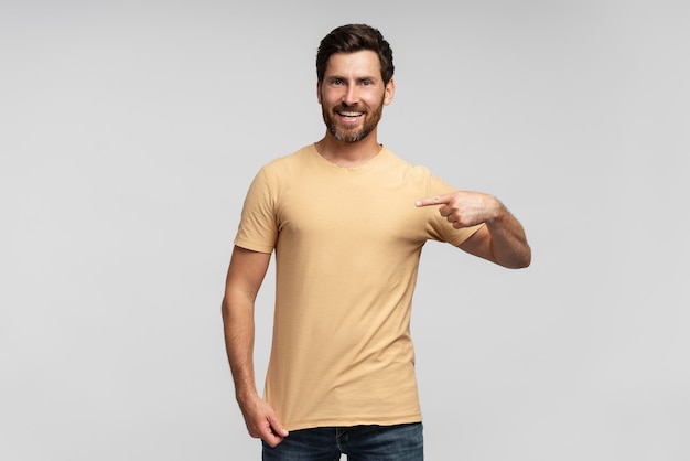 Retrato de um homem sorridente, bonito e barbudo, um hipster vestindo uma camiseta em branco apontando para si mesmo.