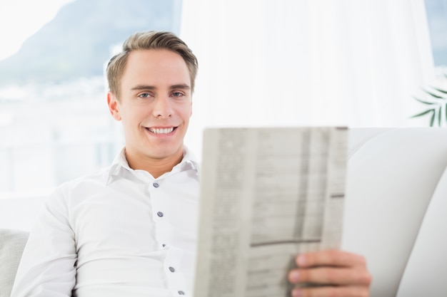 Retrato de um homem sorridente lendo jornal no sofá