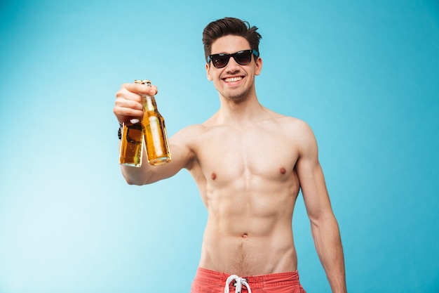 Retrato de um homem sorridente sem camisa mostrando uma garrafa de cerveja