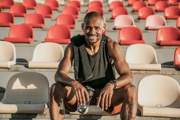 Retrato de um homem sorridente, sentado nos assentos do estádio, relaxe após o treino