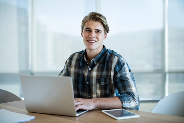 Retrato de um homem sorridente trabalhando em um laptop no escritório