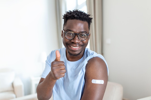 Retrato de um homem sorrindo depois de receber uma vacina Homem africano segurando a manga da camisa e mostrando o braço com curativo após receber a vacinação