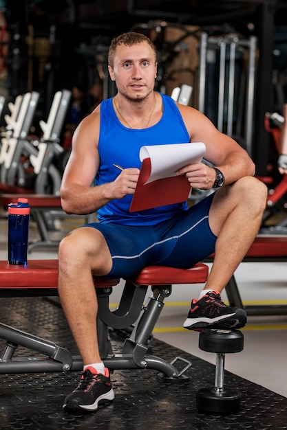 Retrato de um homem um personal trainer segurando uma prancheta com um plano de treinamento no ginásio