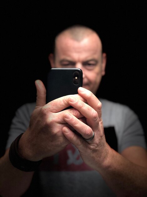 Foto retrato de um homem usando um telefone celular contra um fundo preto