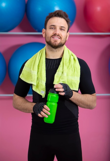 Foto retrato de um homem vestindo roupas esportivas segurando uma garrafa de água no ginásio