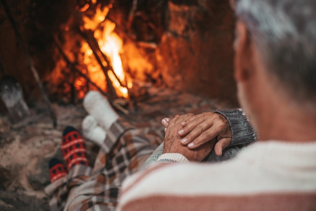 Retrato de um idoso maduro bonito curtindo o natal em frente à lareira quente em casa sentindo frio abraçando juntos e segurando as mãos usando meias coloridas de férias nos pésxa