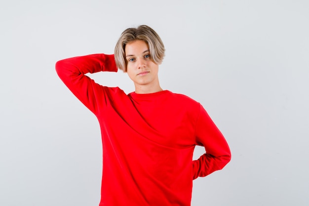 Retrato de um jovem adolescente com a mão atrás da cabeça em um suéter vermelho e olhando a vista frontal confiante