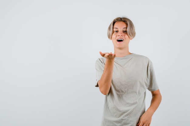 Retrato de um jovem adolescente esticando a mão para a câmera em uma camiseta e olhando de frente para a frente.