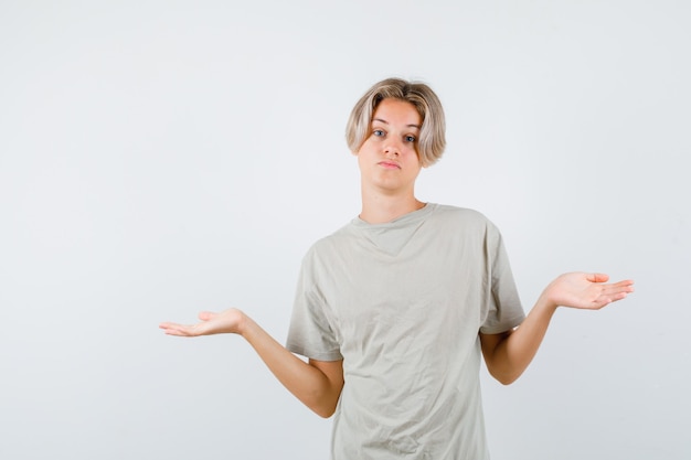 Retrato de um jovem adolescente mostrando um gesto de impotência em uma camiseta e parecendo indeciso com a vista frontal