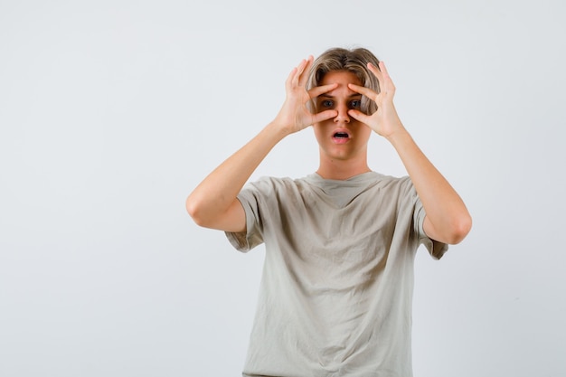 Retrato de um jovem adolescente olhando por entre os dedos em uma camiseta e olhando confuso de frente