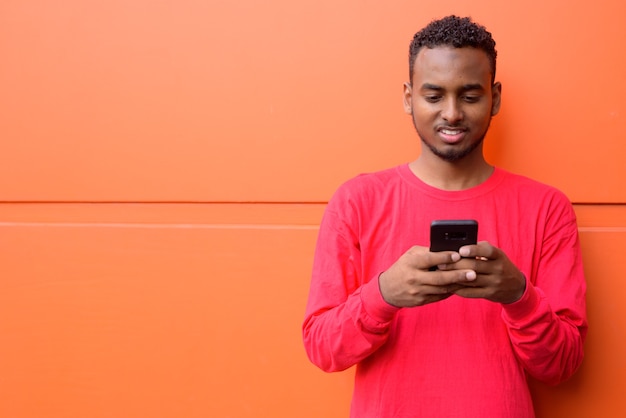 Retrato de um jovem africano bonito barbudo com cabelo afro contra uma parede laranja ao ar livre