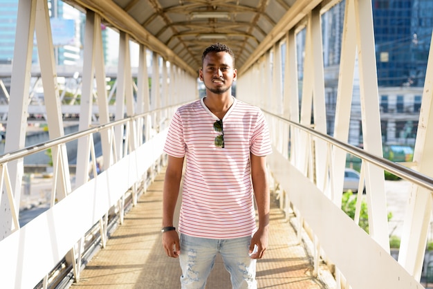 Retrato de um jovem africano bonito, barbudo e cabelo afro, na passarela ao ar livre da cidade