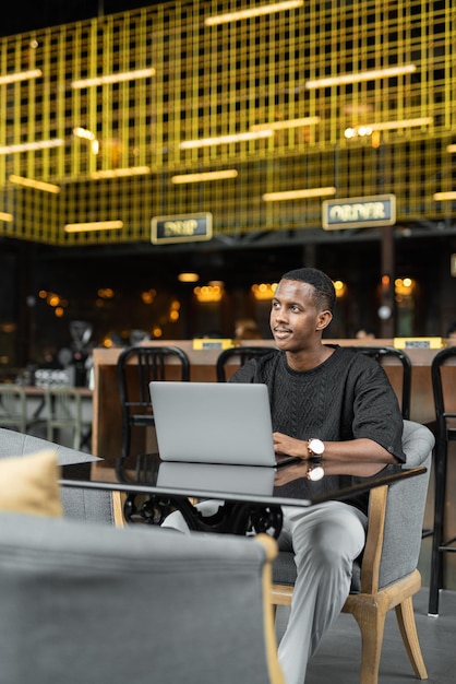 Retrato de um jovem africano bonito usando laptop na cafeteria