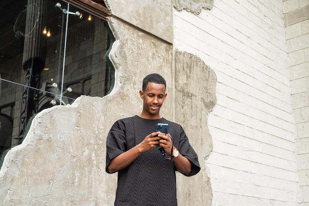 Retrato de um jovem africano bonito usando telefone celular ao ar livre