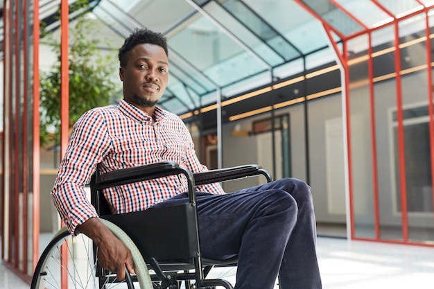 Retrato de um jovem africano com deficiência sentado em uma cadeira de rodas em um prédio comercial