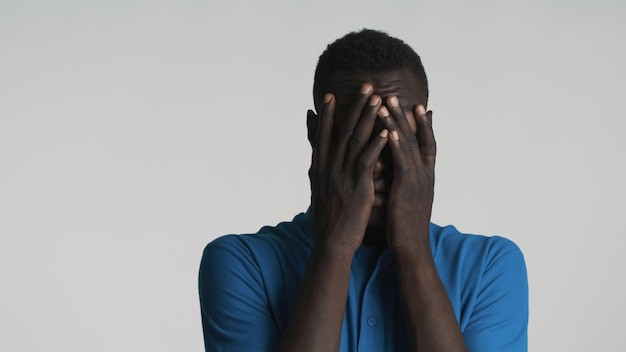 Retrato de um jovem afro-americano cobrindo o rosto com as mãos sobre fundo branco Expressão cansada