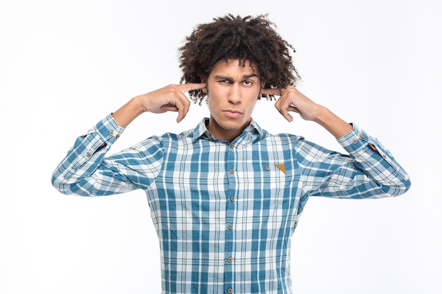 Foto retrato de um jovem afro-americano sério, cobrindo as orelhas isoladas em uma parede branca.