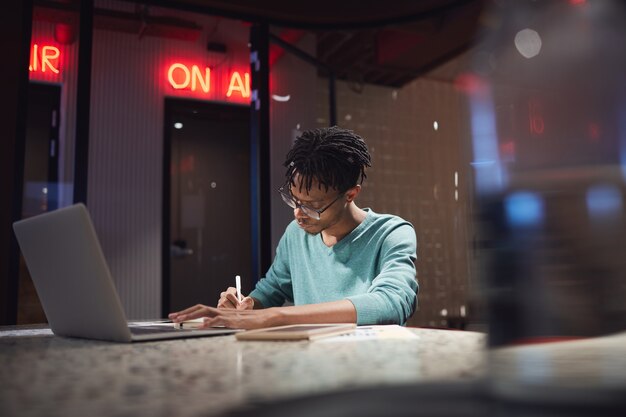 Retrato de um jovem afro-americano trabalhando até tarde em casa ou no escuro do escritório
