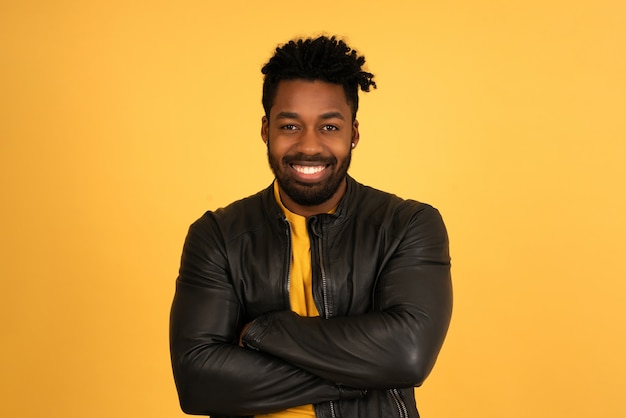 Retrato de um jovem afro olhando para a câmera e sorrindo em pé contra um fundo amarelo isolado.