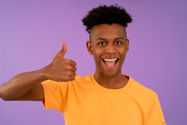 Retrato de um jovem afro, olhando para a câmera e sorrindo enquanto aparecia os polegares.
