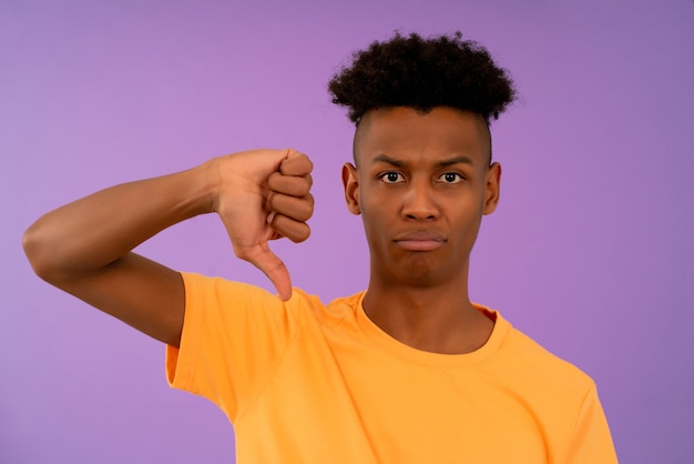 Retrato de um jovem afro, olhando para a câmera enquanto mostra os polegares para baixo.