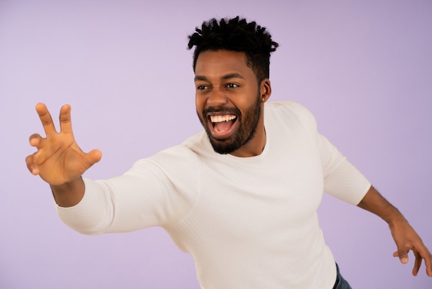 Retrato de um jovem afro sorrindo ao tentar pegar algo com a mão contra um fundo isolado.