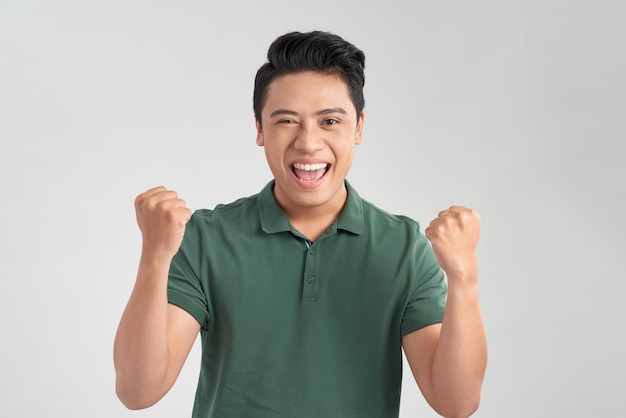 Retrato de um jovem alegre em camiseta verde comemorando o sucesso isolado sobre fundo branco