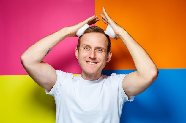 Retrato de um jovem alegre em um fundo multicolorido, vestido com uma camiseta branca, espuma de cabelo derramada nas mãos, cria um penteado da moda