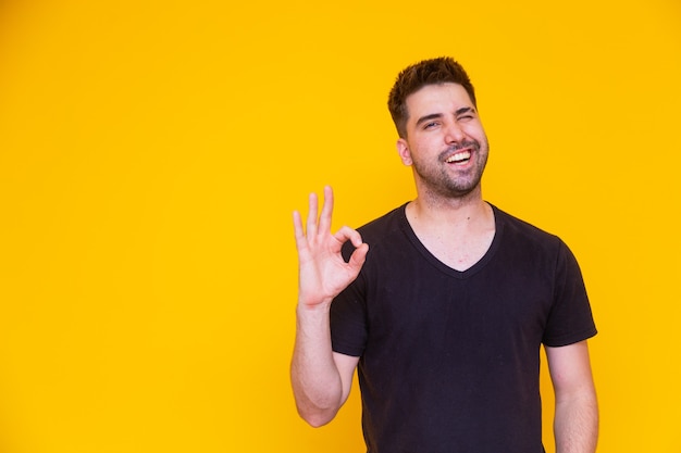 Retrato de um jovem alegre, mostrando um gesto de aprovação isolado em um fundo amarelo.