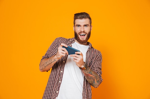 Retrato de um jovem alegre, vestindo roupas casuais, jogando no celular