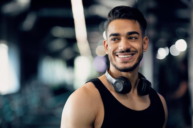 Retrato de um jovem árabe bonito sorridente com fones de ouvido sem fio no pescoço